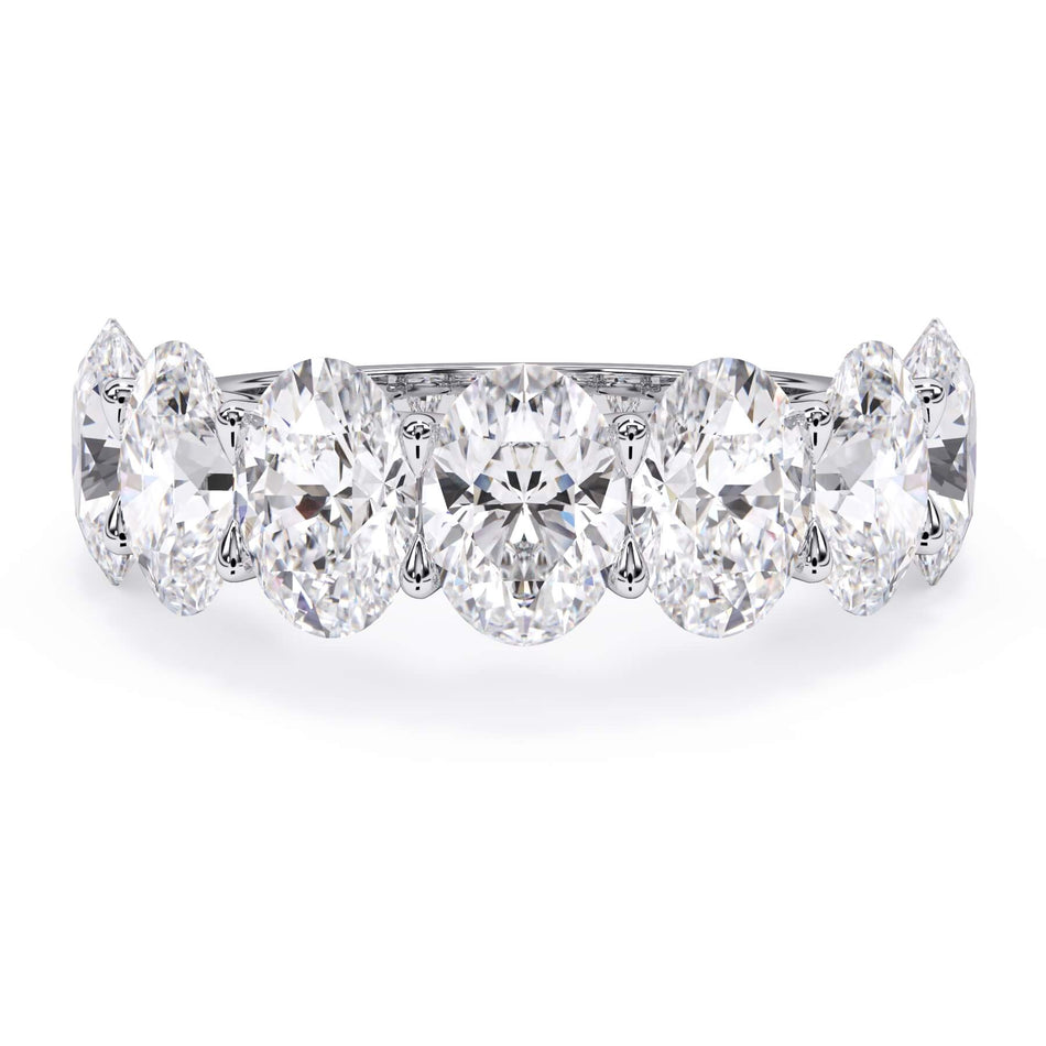 A picture of a seven stone diamond wedding ring with oval shaped diamonds that are U prong set in white gold or platinum on a white background with the ring facing forward, lying down.