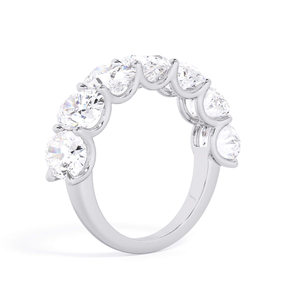 A picture of a seven stone diamond wedding ring with oval shaped diamonds that are U prong set in white gold or platinum on a white background with a slightly angled, through the finger view.