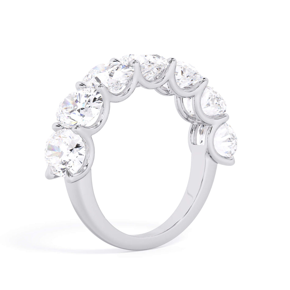 A picture of a seven stone diamond wedding ring with oval shaped diamonds that are U prong set in white gold or platinum on a white background with a slightly angled, through the finger view.