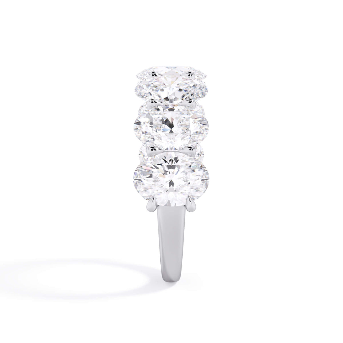 A picture of a seven stone diamond wedding ring with oval shaped diamonds that are U prong set in white gold or platinum on a white background with a side profile view.