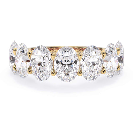 A picture of a seven stone diamond wedding ring with oval shaped diamonds that are U prong set in yellow gold on a white background with the ring facing forward, lying down.