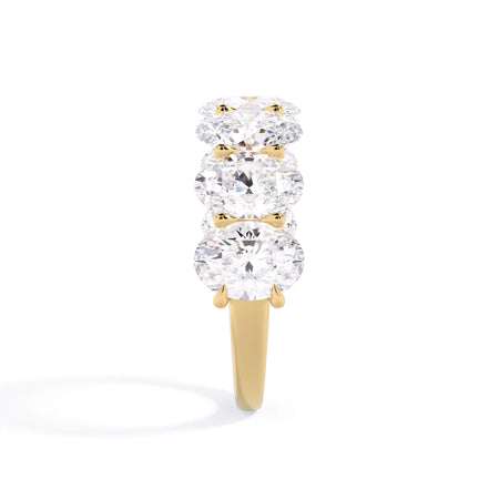 A picture of a seven stone diamond wedding ring with oval shaped diamonds that are U prong set in yellow gold on a white background with a side profile view.