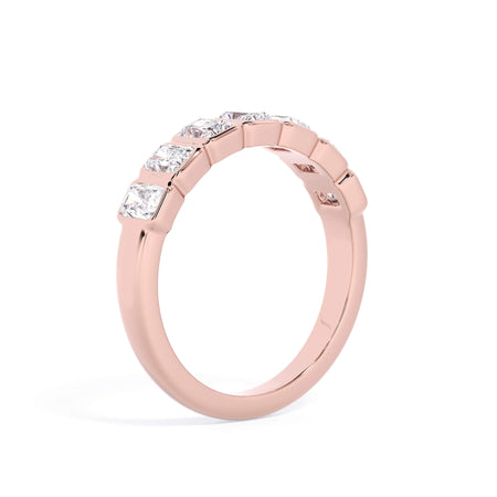 A picture of a seven stone diamond wedding ring with radiant cut diamonds that are bezel set in rose gold on a white background with the ring facing forward, lying down.