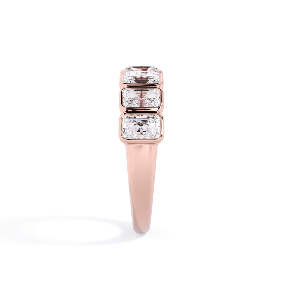 A picture of a seven stone diamond wedding ring with radiant cut diamonds that are bezel set in rose gold on a white background with a side profile view.