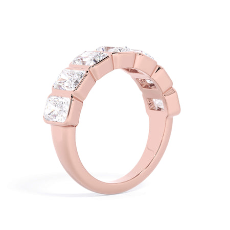 A picture of a seven stone diamond wedding ring with radiant cut diamonds that are bezel set in rose gold on a white background with a slightly angled, through the finger view.