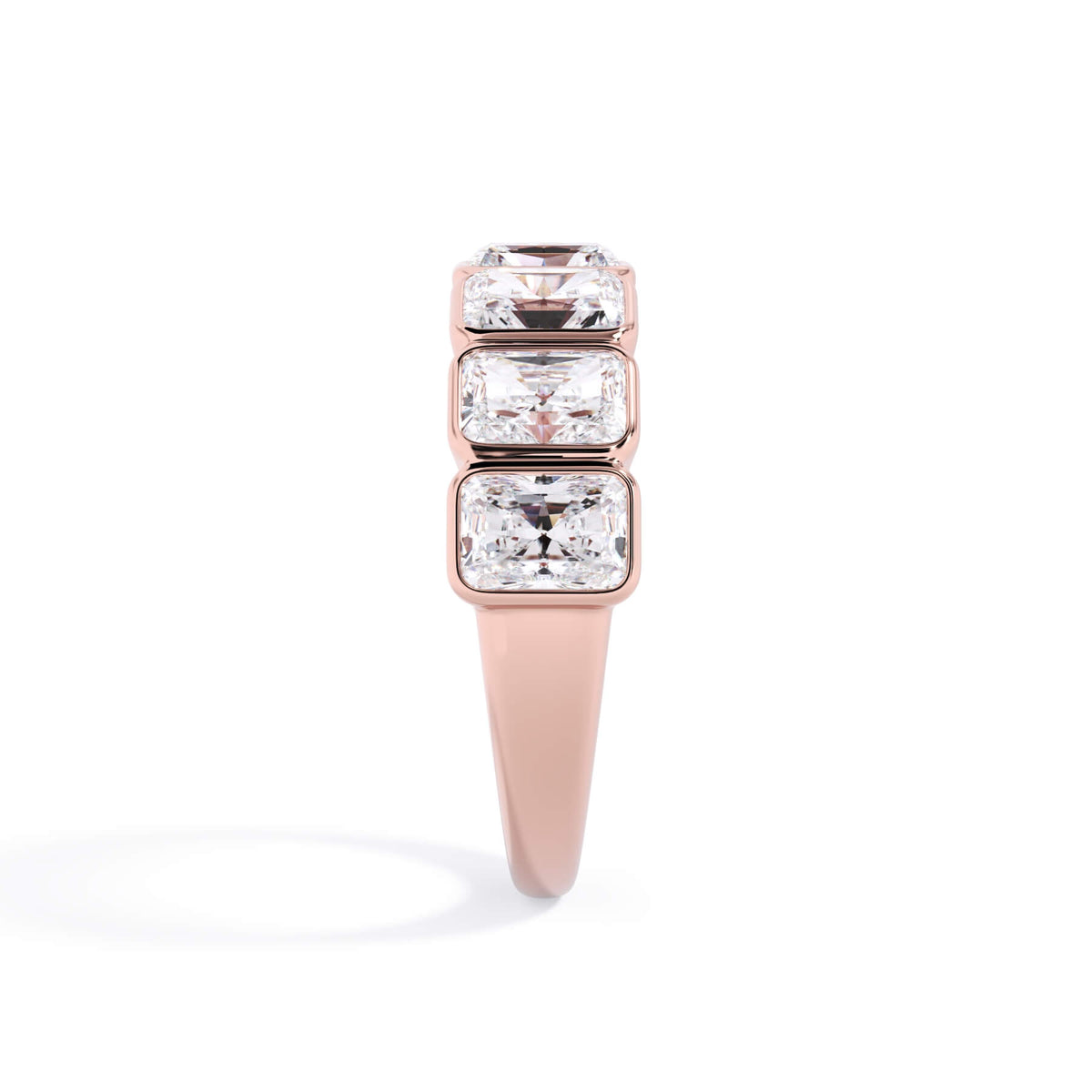 A picture of a seven stone diamond wedding ring with radiant cut diamonds that are bezel set in rose gold on a white background with a side profile view.