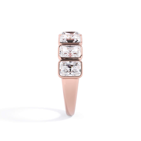 A picture of a seven stone diamond wedding ring with radiant cut diamonds that are bezel set in rose gold on a white background with a side profile view.