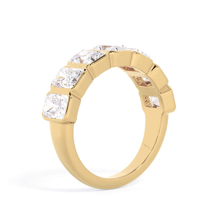 A picture of a seven stone diamond wedding ring with radiant cut diamonds that are bezel set in yellow gold on a white background with a slightly angled, through the finger view.