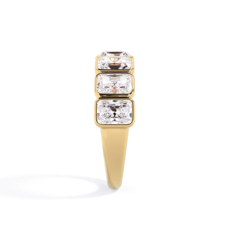 A picture of a seven stone diamond wedding ring with radiant cut diamonds that are bezel set in yellow gold on a white background with a side profile view.