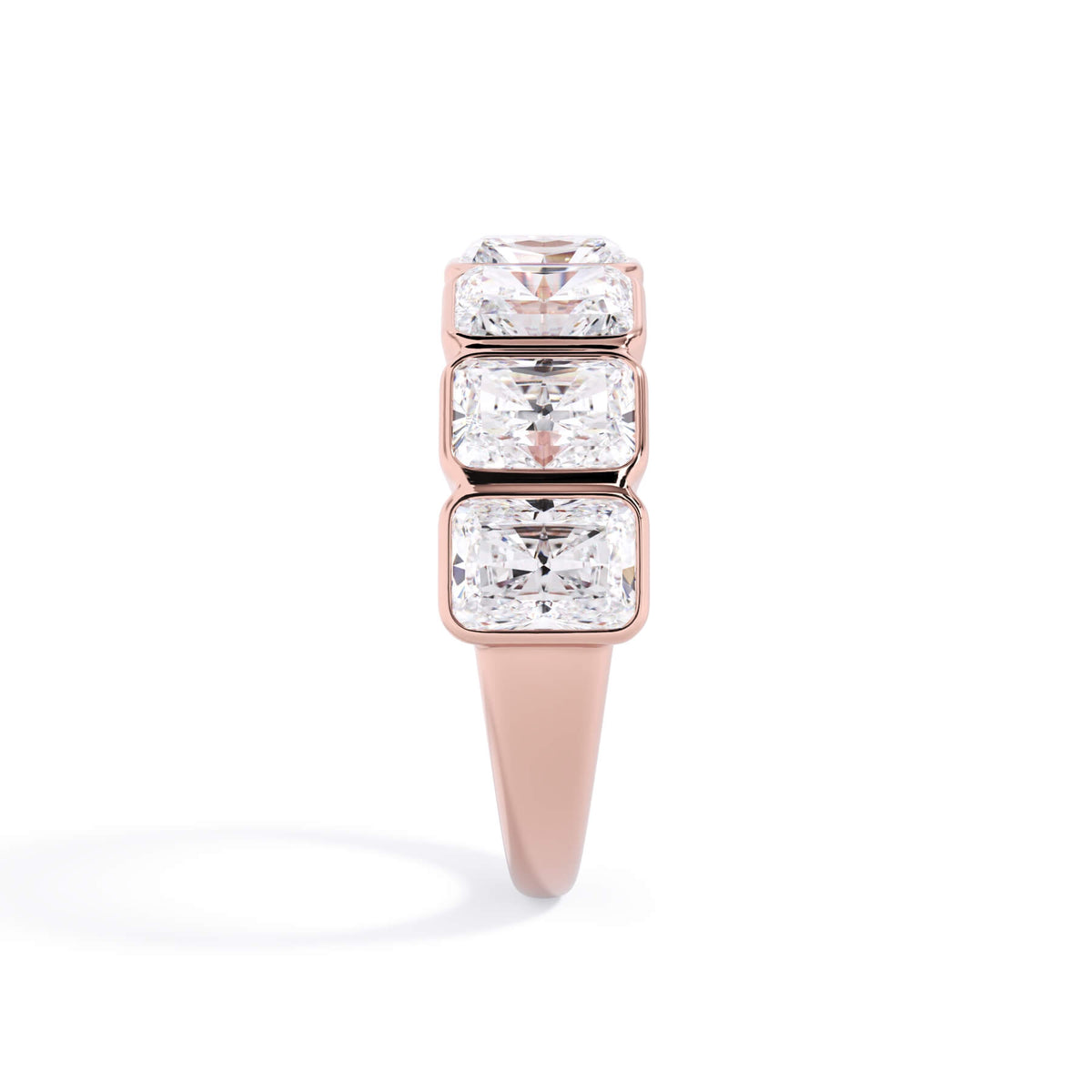 A picture of a seven stone diamond wedding ring with radiant cut diamonds that are bezel set in rose gold on a white background with a side profile view.
