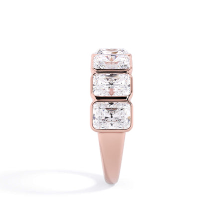 A picture of a seven stone diamond wedding ring with radiant cut diamonds that are bezel set in rose gold on a white background with a side profile view.