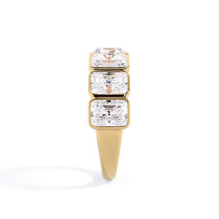 A picture of a seven stone diamond wedding ring with radiant cut diamonds that are bezel set in yellow gold on a white background with a side profile view.