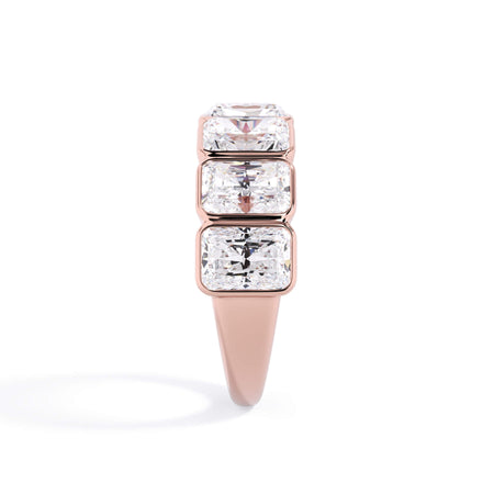 A picture of a seven stone diamond wedding ring with radiant cut diamonds that are bezel set in rose gold on a white background with a side profile view.