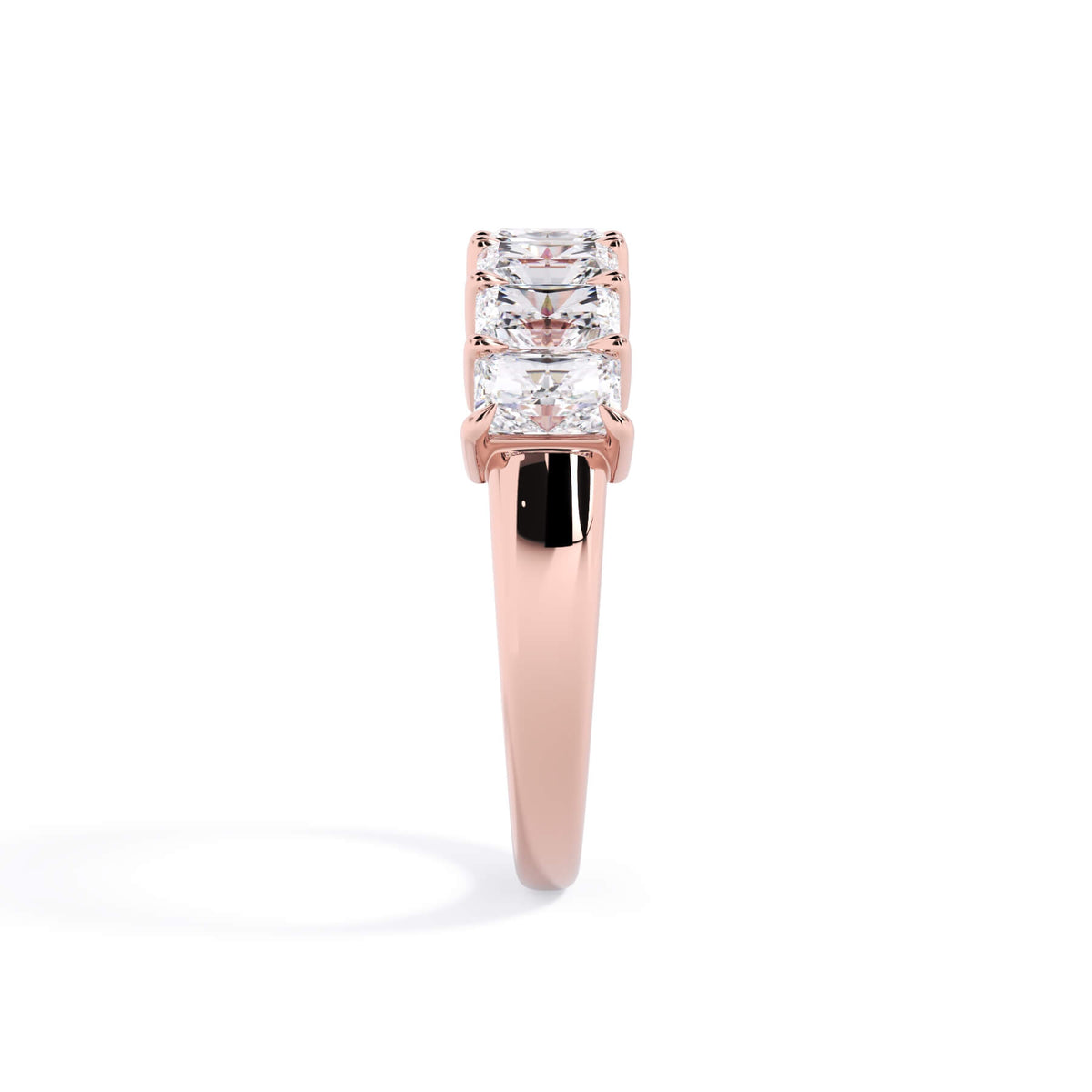 A picture of a seven stone diamond wedding ring with radiant cut diamonds that are shared prong set in rose gold on a white background with a side profile view.