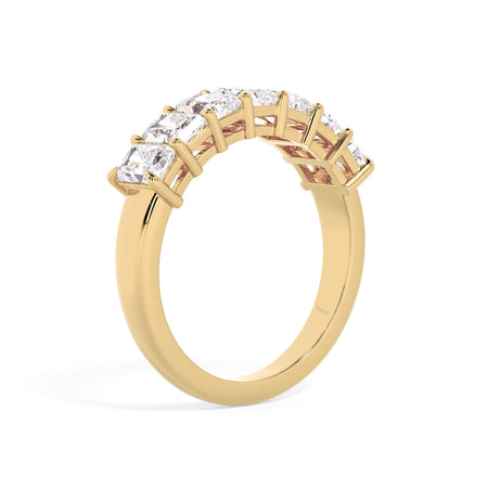 A picture of a seven stone diamond wedding ring with radiant cut diamonds that are shared prong set in yellow gold on a white background with a slightly angled, through the finger view.