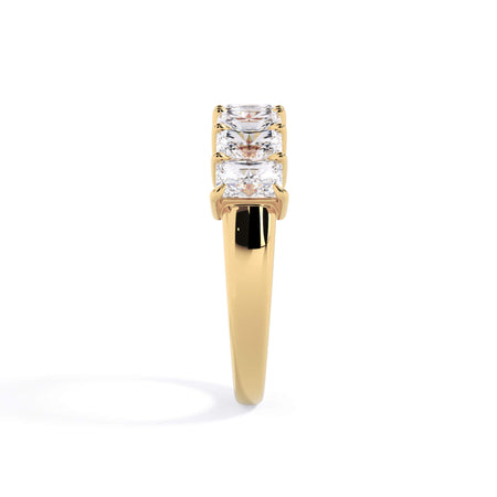 A picture of a seven stone diamond wedding ring with radiant cut diamonds that are shared prong set in yellow gold on a white background with a side profile view.