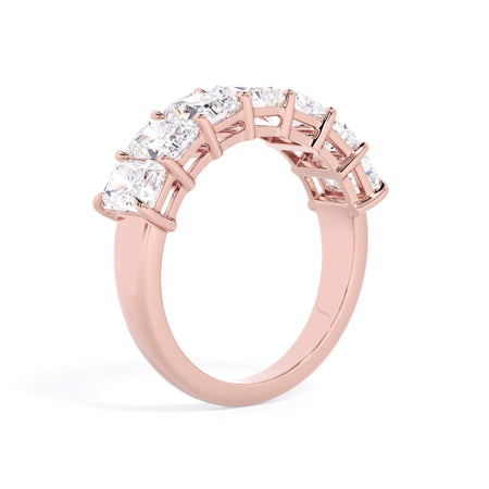 A picture of a seven stone diamond wedding ring with radiant cut diamonds that are shared prong set in rose gold on a white background with a slightly angled, through the finger view.