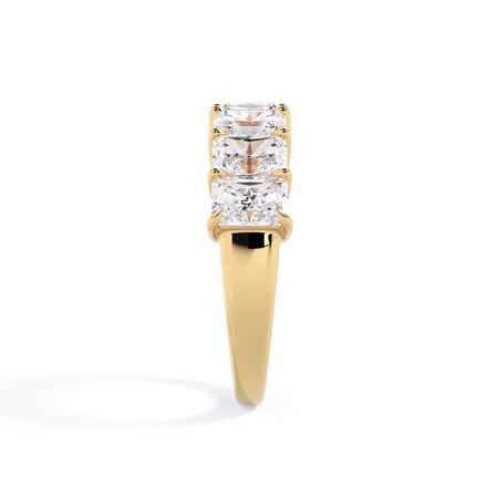A picture of a seven stone diamond wedding ring with radiant cut diamonds that are shared prong set in yellow gold on a white background with a side profile view.