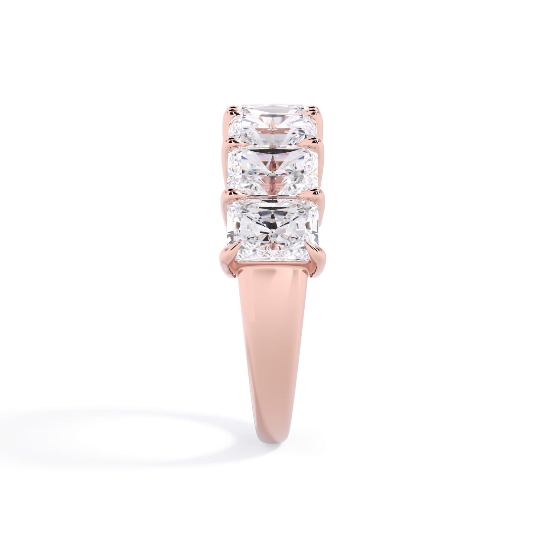 A picture of a seven stone diamond wedding ring with radiant cut diamonds that are shared prong set in rose gold on a white background with a side profile view.
