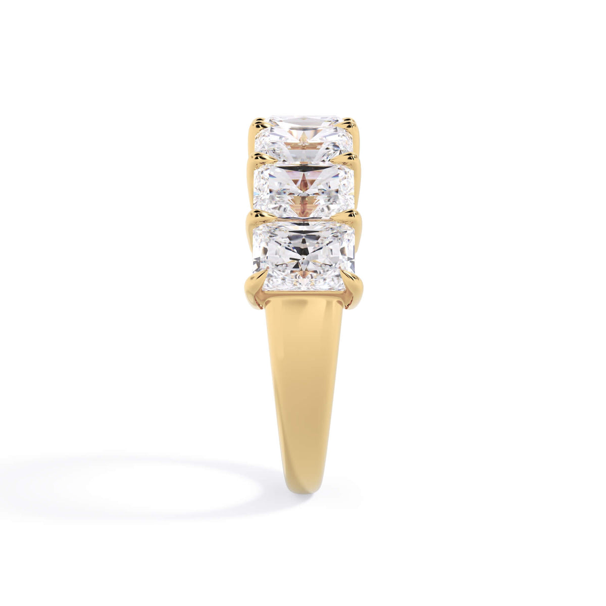 A picture of a seven stone diamond wedding ring with radiant cut diamonds that are shared prong set in yellow gold on a white background with a side profile view.