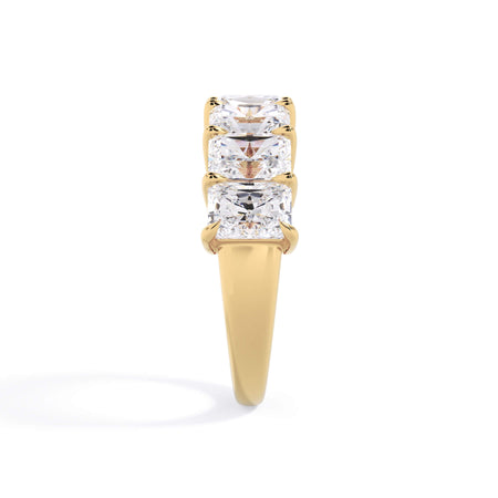 A picture of a seven stone diamond wedding ring with radiant cut diamonds that are shared prong set in yellow gold on a white background with a side profile view.
