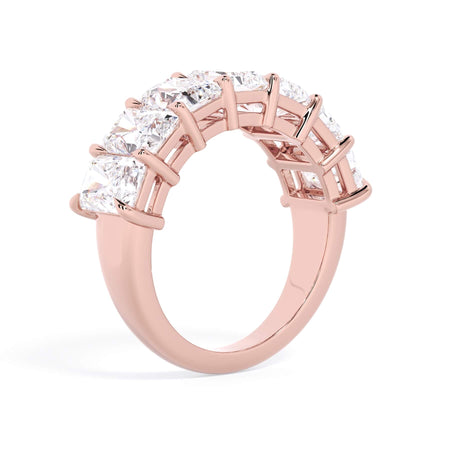 A picture of a seven stone diamond wedding ring with radiant cut diamonds that are shared prong set in rose gold on a white background with a slightly angled, through the finger view.