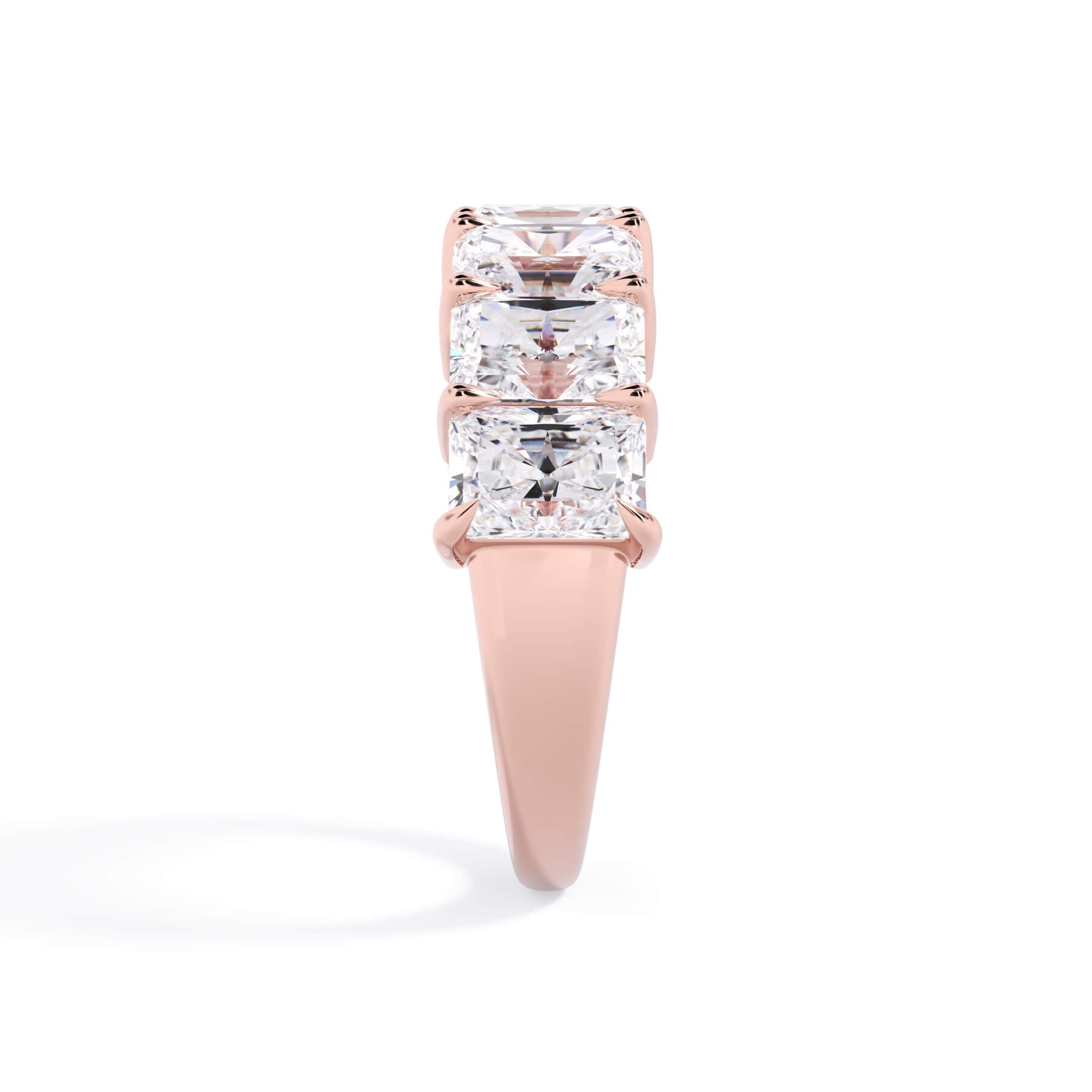 A picture of a seven stone diamond wedding ring with radiant cut diamonds that are shared prong set in rose gold on a white background with a side profile view.