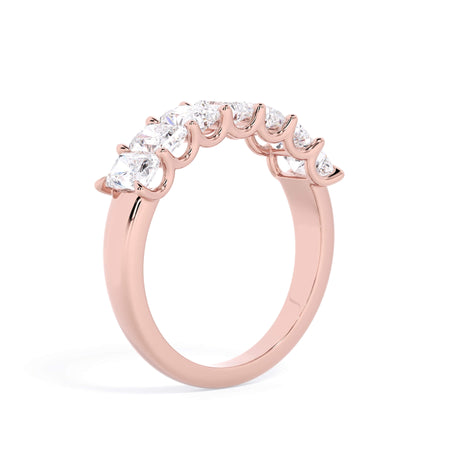 A picture of a seven stone diamond wedding ring with radiant cut diamonds that are U prong set in rose gold on a white background with a slightly angled, through the finger view.