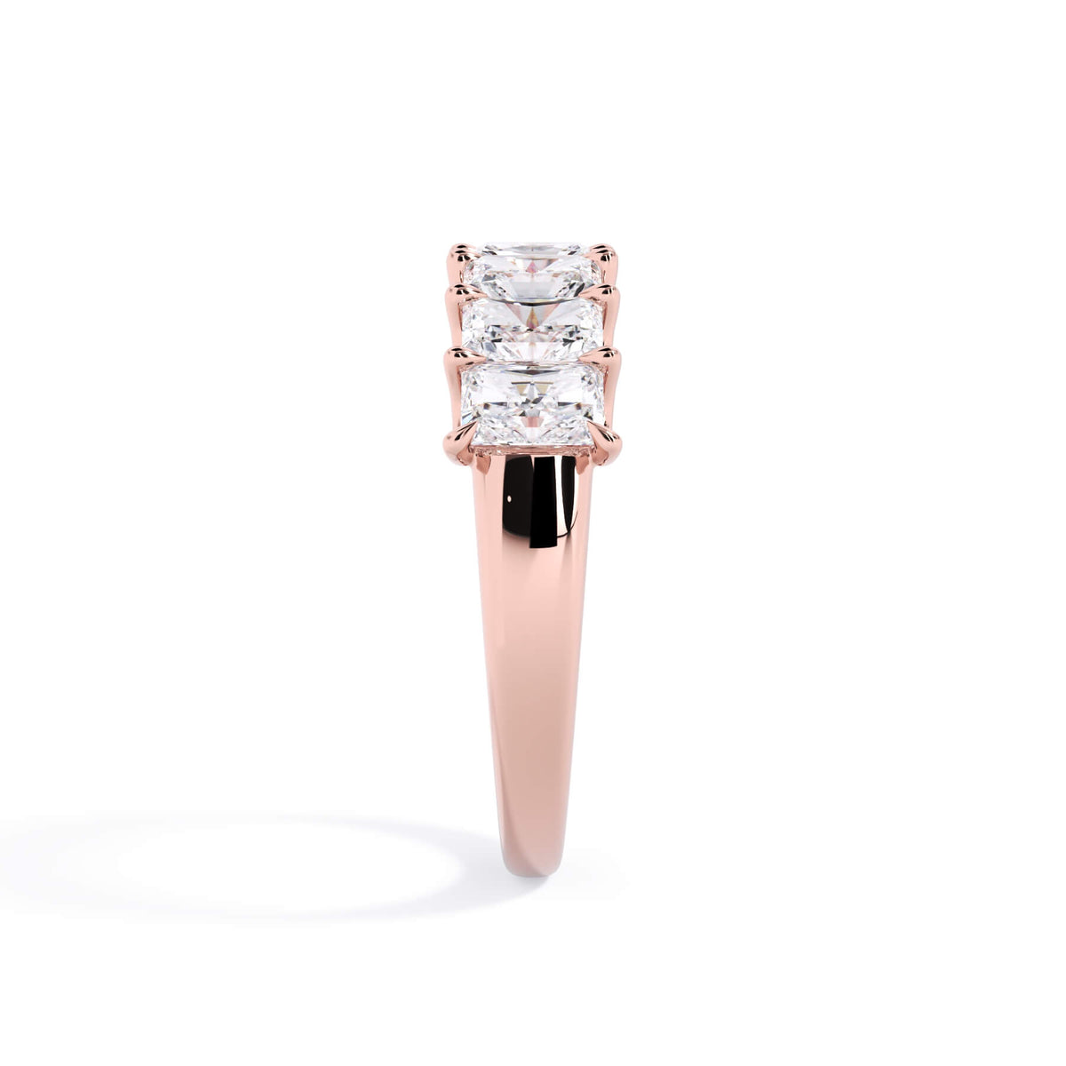 A picture of a seven stone diamond wedding ring with radiant cut diamonds that are U prong set in rose gold on a white background with a side profile view.