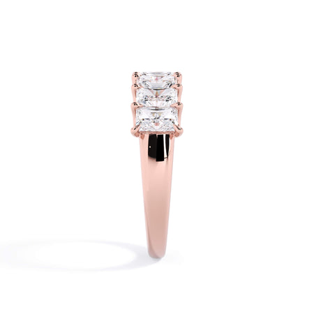 A picture of a seven stone diamond wedding ring with radiant cut diamonds that are U prong set in rose gold on a white background with a side profile view.