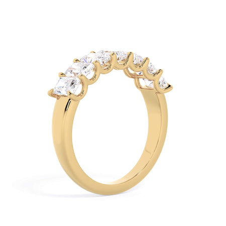 A picture of a seven stone diamond wedding ring with radiant cut diamonds that are U prong set in yellow gold on a white background with a slightly angled, through the finger view.