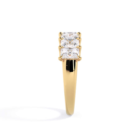 A picture of a seven stone diamond wedding ring with radiant cut diamonds that are U prong set in yellow gold on a white background with a side profile view.