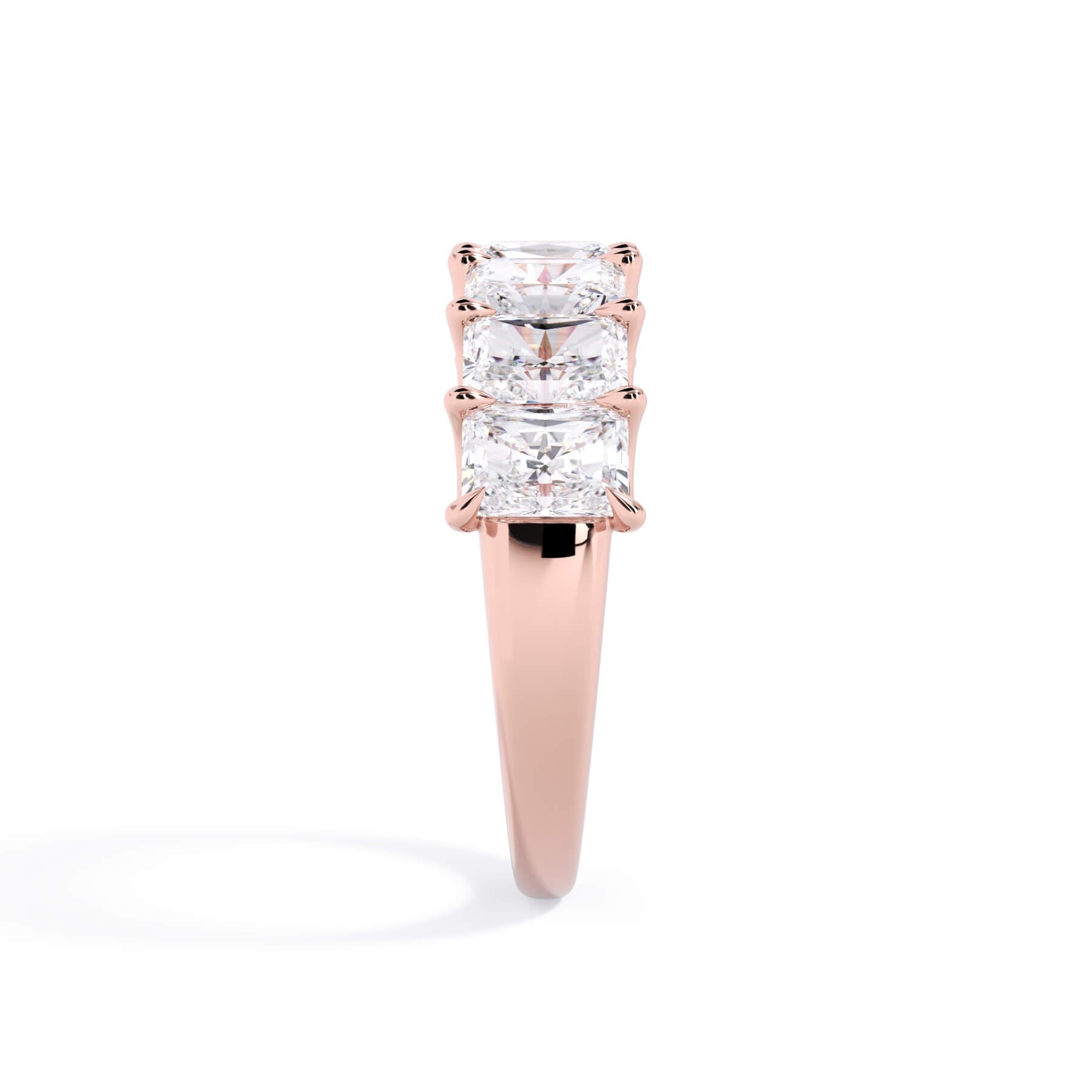 A picture of a seven stone diamond wedding ring with radiant cut diamonds that are U prong set in rose gold on a white background with a side profile view.