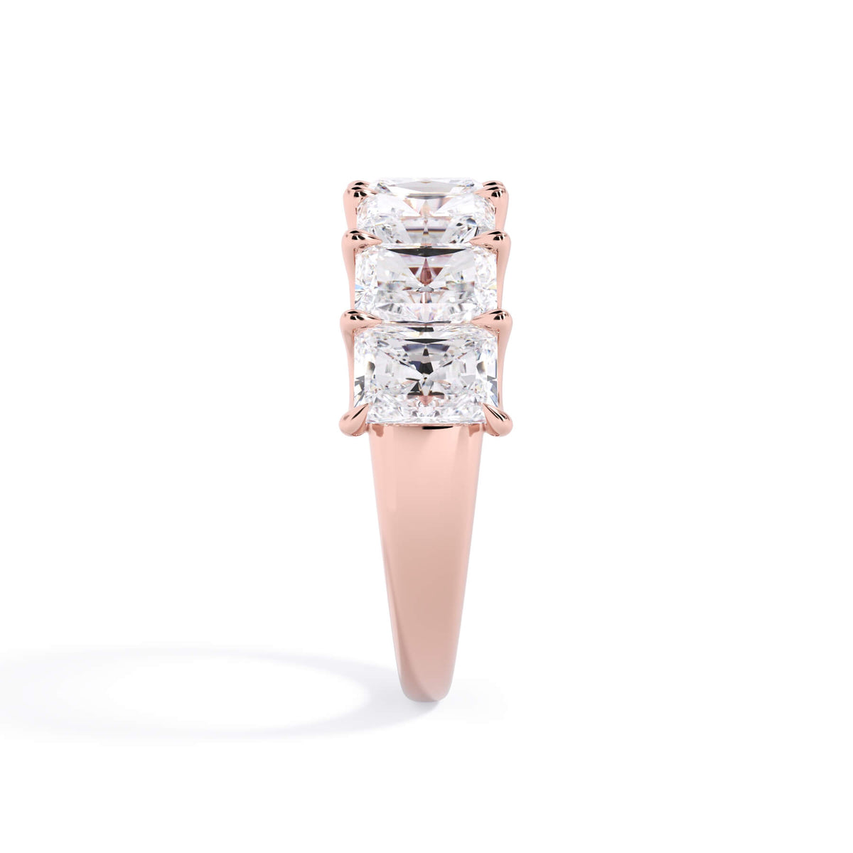 A picture of a seven stone diamond wedding ring with radiant cut diamonds that are U prong set in rose gold on a white background with the ring facing forward, lying down.