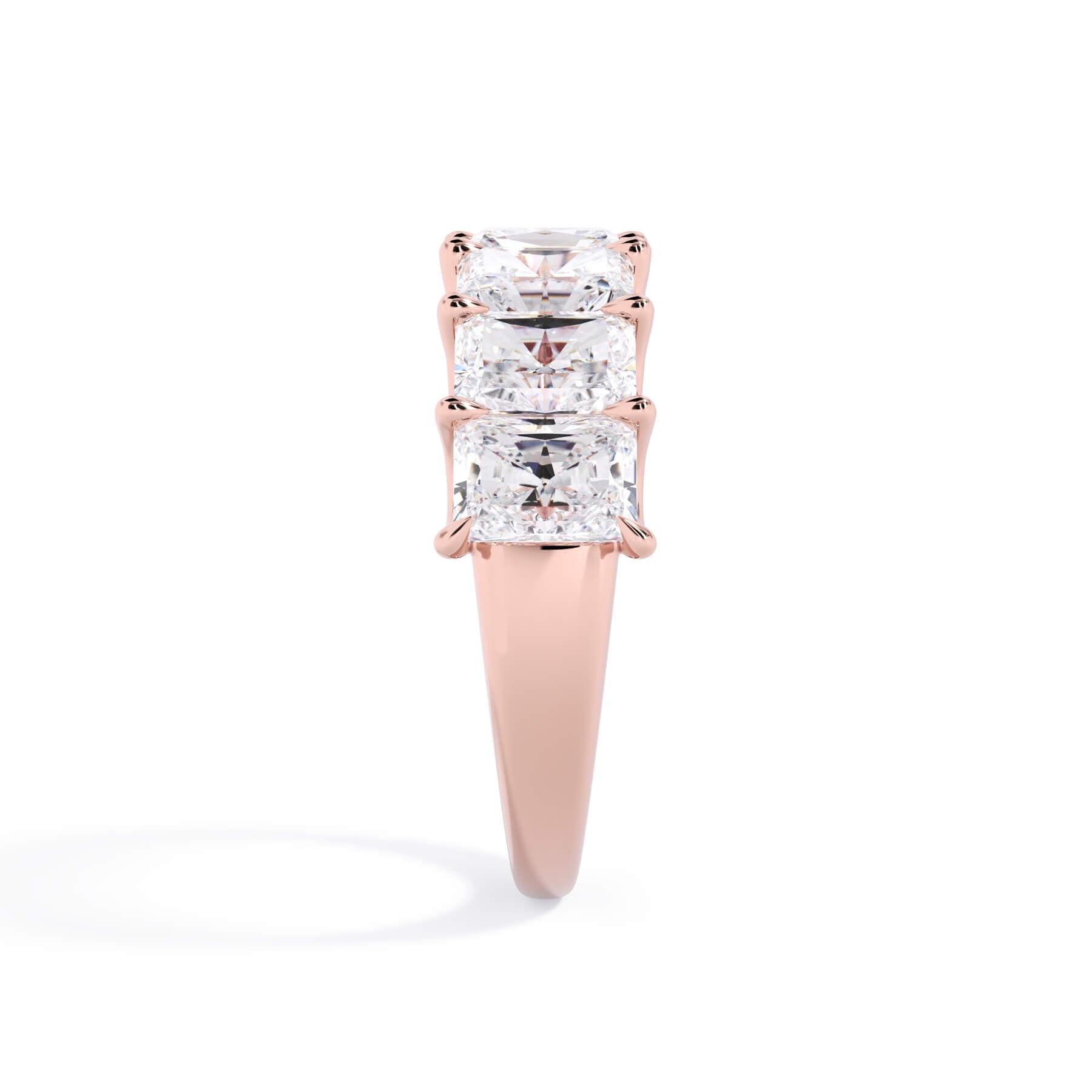 A picture of a seven stone diamond wedding ring with radiant cut diamonds that are U prong set in rose gold on a white background with the ring facing forward, lying down.