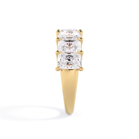 A picture of a seven stone diamond wedding ring with radiant cut diamonds that are U prong set in yellow gold on a white background with a side profile view.