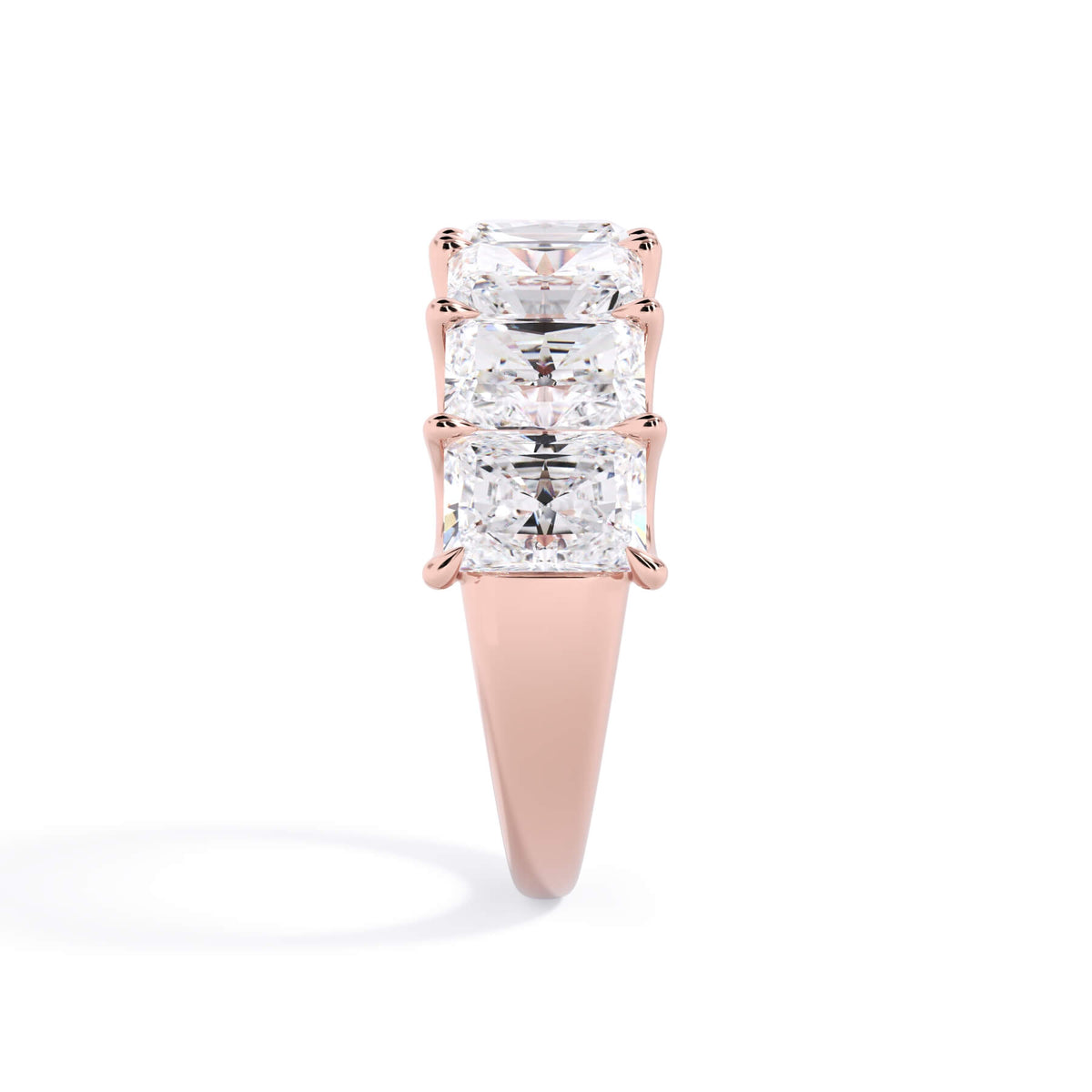 A picture of a seven stone diamond wedding ring with radiant cut diamonds that are U prong set in rose gold on a white background with a side profile view.