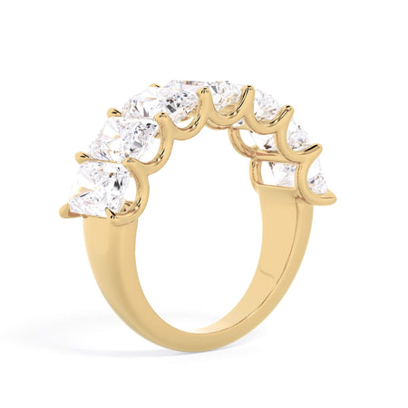 A picture of a seven stone diamond wedding ring with radiant cut diamonds that are U prong set in yellow gold on a white background with a slightly angled, through the finger view.