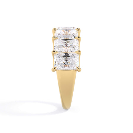 A picture of a seven stone diamond wedding ring with radiant cut diamonds that are U prong set in yellow gold on a white background with a side profile view.