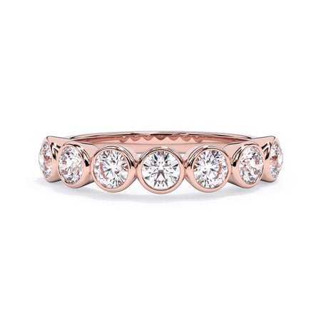 A picture of a seven stone diamond wedding ring with round diamonds that are bezel set in rose gold on a white background with the ring facing forward, lying down.