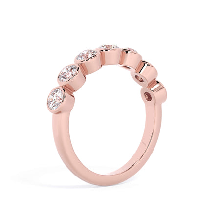 A picture of a seven stone diamond wedding ring with round diamonds that are bezel set in rose gold on a white background with a slightly angled, through the finger view.