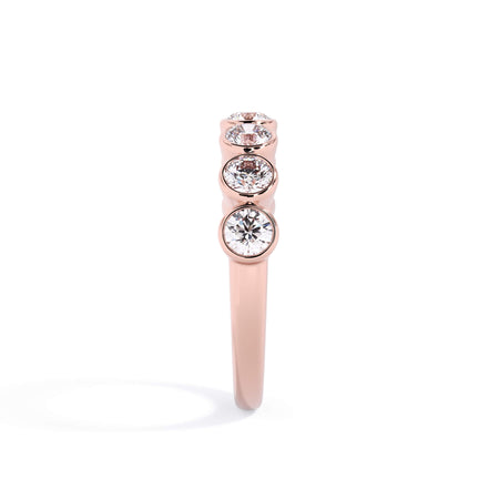 A picture of a seven stone diamond wedding ring with round diamonds that are bezel set in rose gold on a white background with a side profile view.