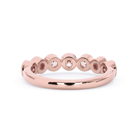 A picture of a seven stone diamond wedding ring with round diamonds that are bezel set in rose gold on a white background with a view of the underside of the ring.
