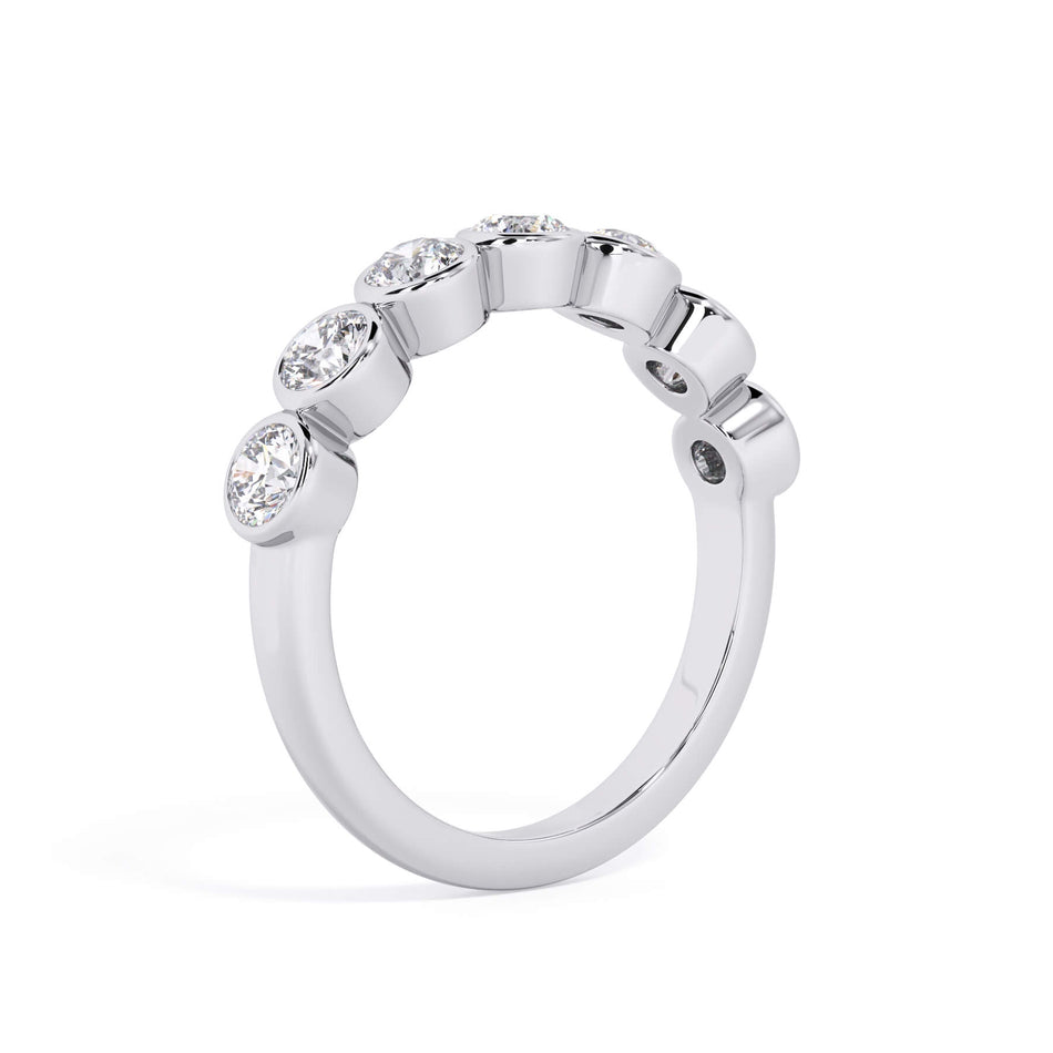 A picture of a seven stone diamond wedding ring with round diamonds that are bezel set in white gold or platinum on a white background with a slightly angled, through the finger view.