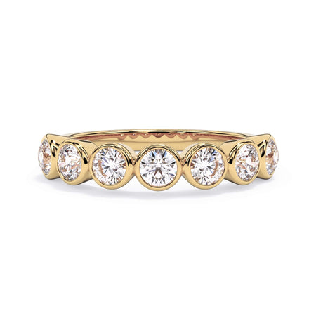 A picture of a seven stone diamond wedding ring with round diamonds that are bezel set in yellow gold on a white background with the ring facing forward, lying down.