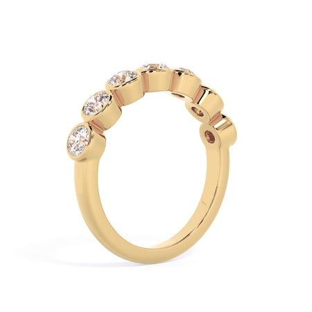 A picture of a seven stone diamond wedding ring with round diamonds that are bezel set in yellow gold on a white background with a slightly angled, through the finger view.