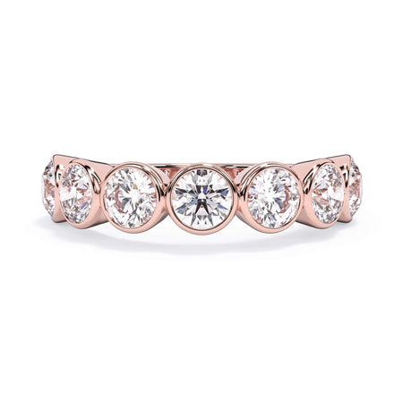 A picture of a seven stone diamond wedding ring with round diamonds that are bezel set in rose gold on a white background with the ring facing forward, lying down.