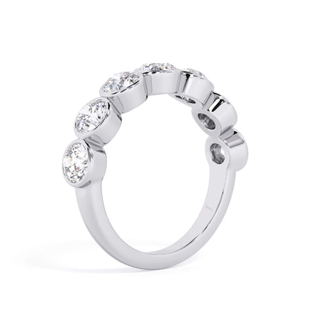 A picture of a seven stone diamond wedding ring with round diamonds that are bezel set in white gold or platinum on a white background with a slightly angled, through the finger view.