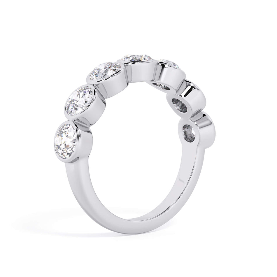 A picture of a seven stone diamond wedding ring with round diamonds that are bezel set in white gold or platinum on a white background with a slightly angled, through the finger view.