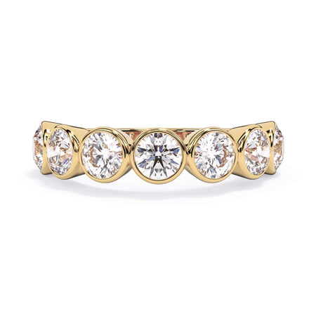 A picture of a seven stone diamond wedding ring with round diamonds that are bezel set in yellow gold on a white background with the ring facing forward, lying down.